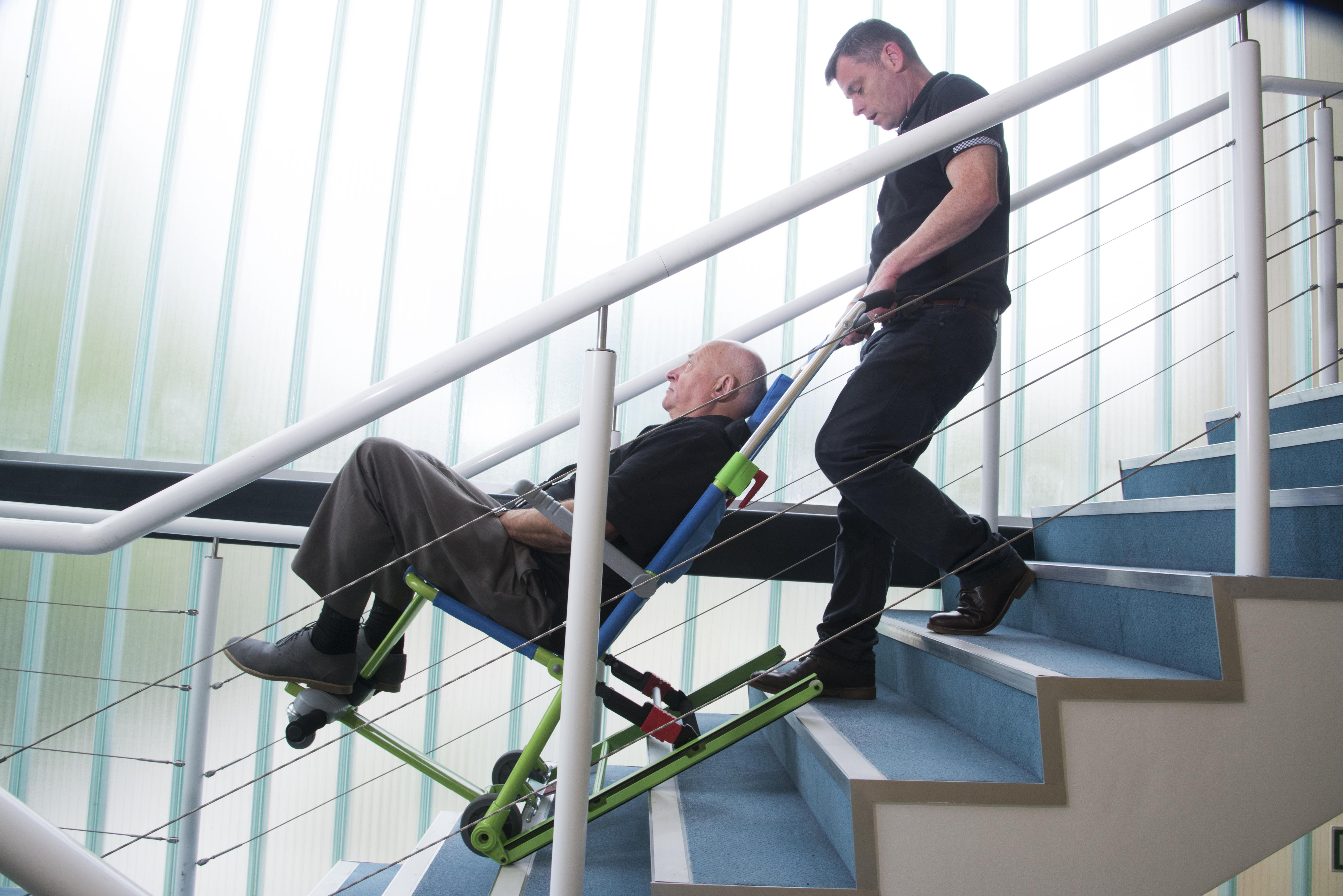 Un aidant évacue une personne à mobilité réduite par les escaliers avec la chaise d'évacuation Excel.