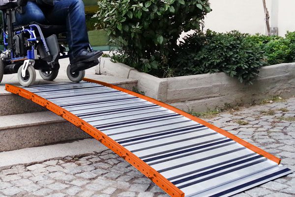 Personne en fauteuil roulant franchissant deux marches grâce une rampe en aluminium Roll Up