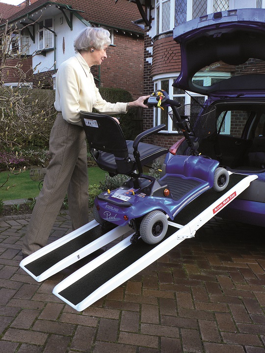 Une sénior charge un scooter électrique dans le coffre d'une voiture grâce à la rampe double pliante de chargement.