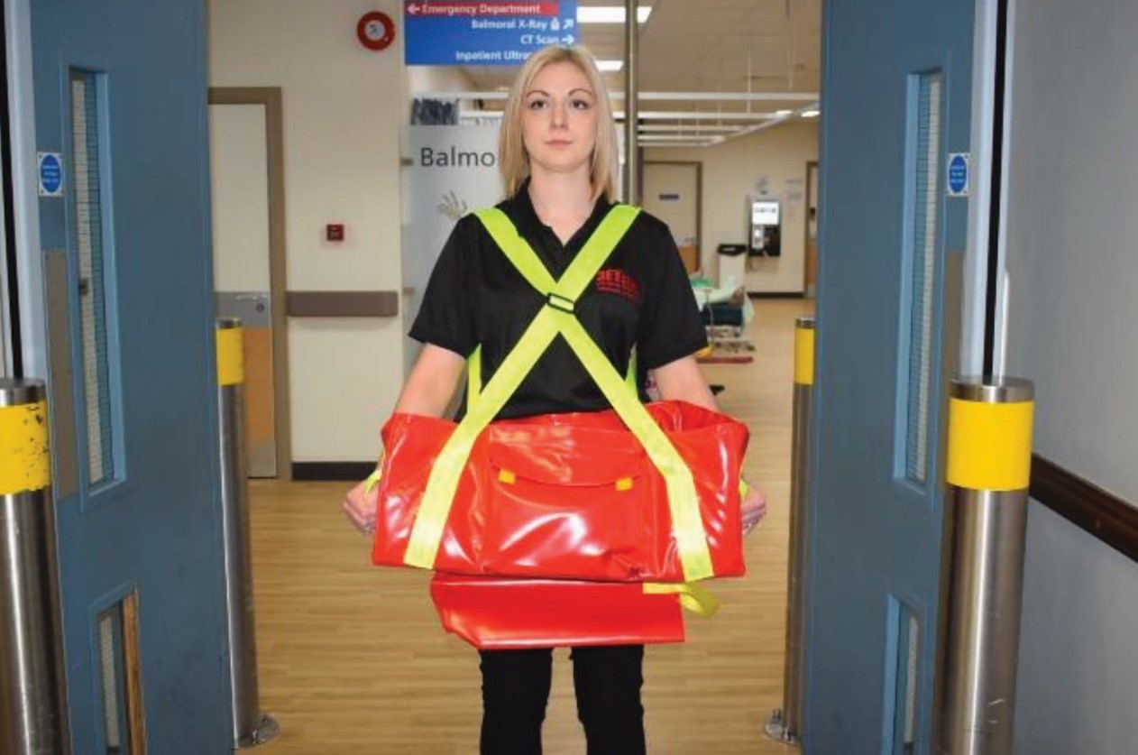 Une femme secouriste portant un EvacBot (couffin permettant l'évacuation des nourrissons) passe les portes battantes d'un hôpital.