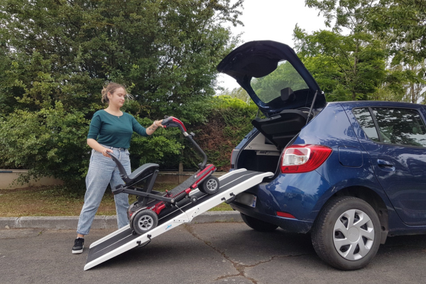 Une jeune femme charge un scooter électrique dans le coffre de sa voiture grâce à sa Scooter Ramp démontable.