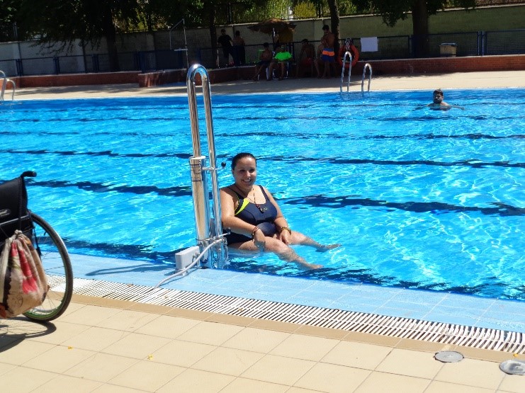 Une dame à mobilité réduite actionne le levier de la potence Isis PK afin de descendre dans la piscine et profiter des loisirs aquatiques.