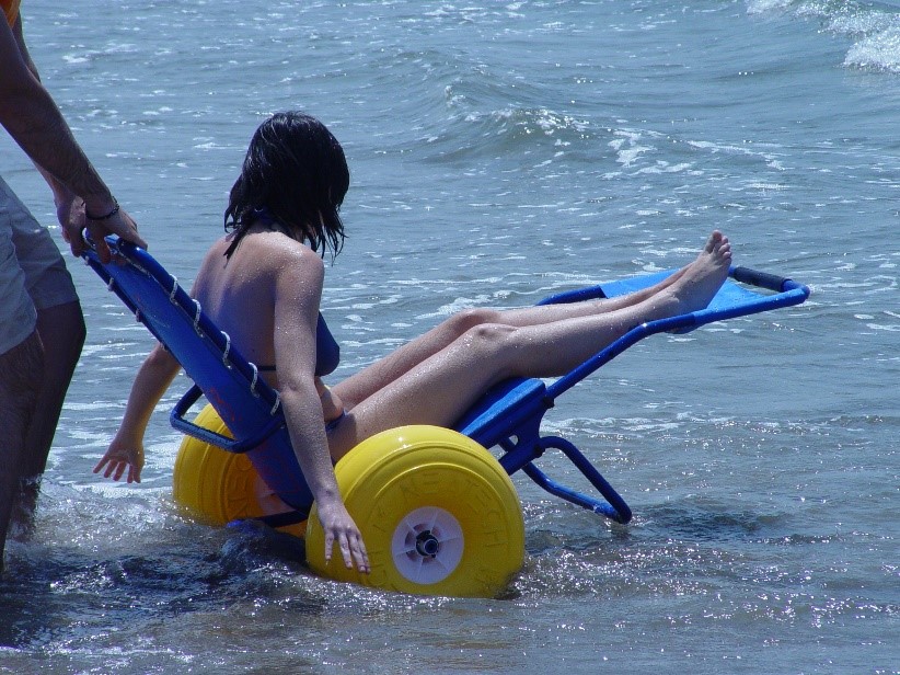 Un homme accompagne une personne à mobilité réduite assise sur un fauteuil J.O.B Classic à entrer dans la mer