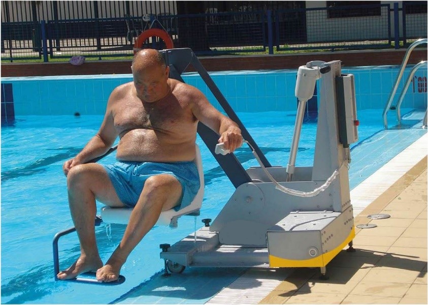 Un homme à mobilité réduite actionne la télécommande de l'élévateur mobile M400 afin de descendre dans l'eau de la piscine.