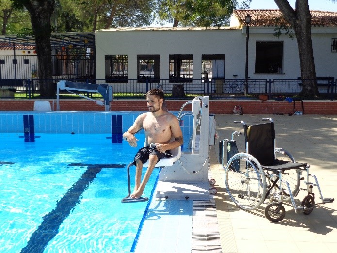 Un jeune homme en situation de handicap actionne la télécommande de l'élévateur fixe M600 afin de descendre en toute autonomie dans le bassin de la piscine.