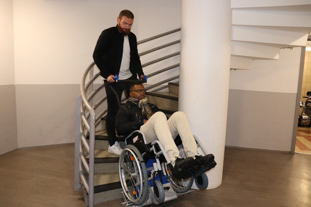 Une personne manipule un monte-escalier PTU sur lequel se trouve une personne à mobilité réduite dans des escaliers colimaçons.