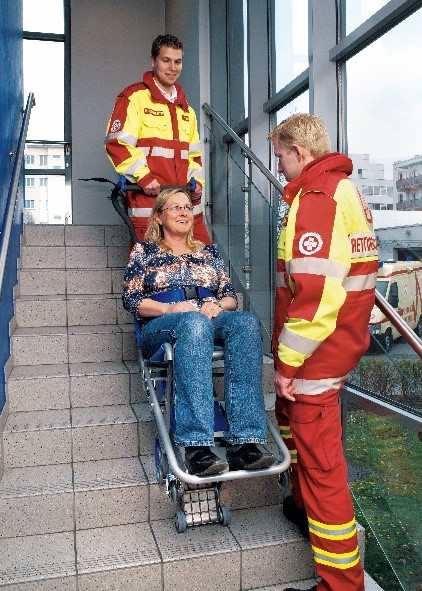 Des secouristes transportent dans un escalier une personne à mobilité réduite sur un monte-escaliers Liftkar PT Fold