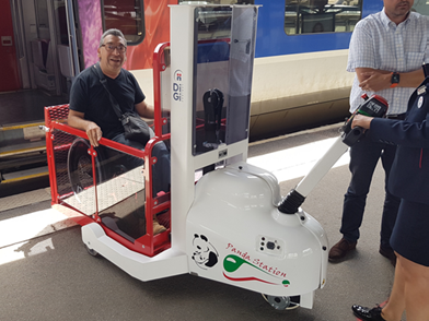 Une membre du personnel d'une gare ferroviaire manipule la plateforme élévatrice verticale Panda Station pour faire descendre du train un homme en fauteuil roulant manuel