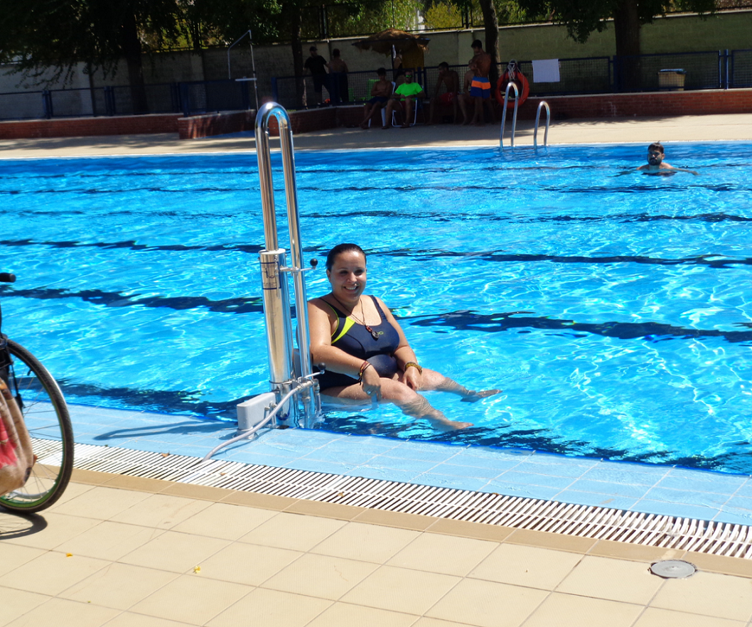 Une dame à mobilité réduite actionne le levier de la potence Isis PK afin de descendre dans la piscine et profiter des loisirs aquatiques.