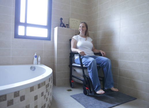 Une femme à mobilité réduite est assise sur le fauteuil d'aisance BathMobile qui s'est glissé au dessus de toilettes existantes.