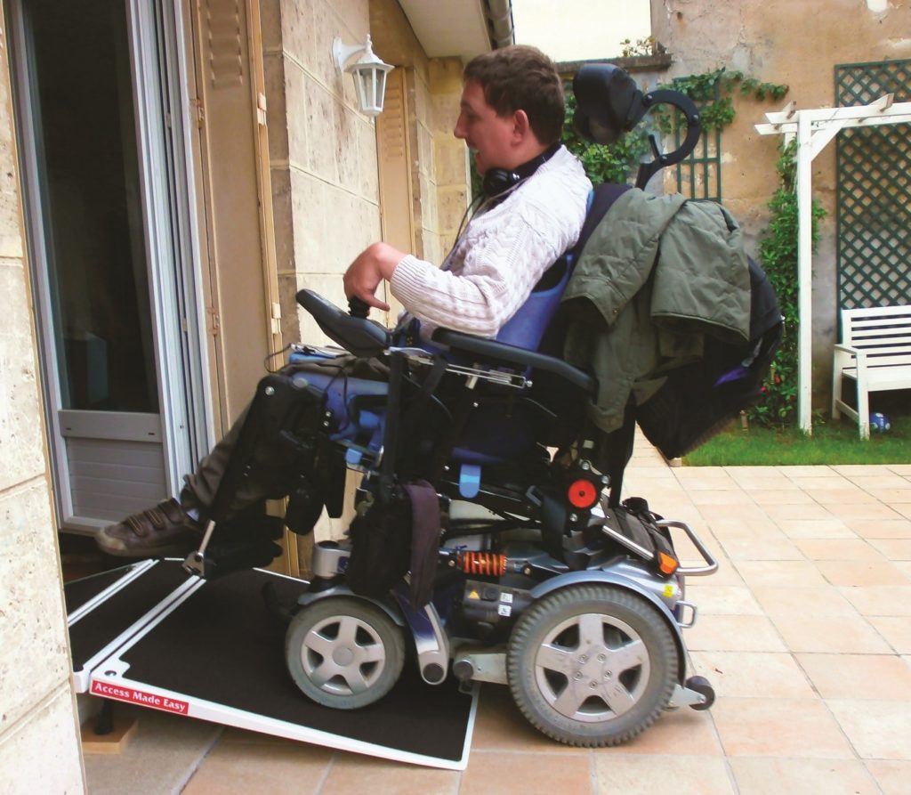 personne en fauteuil passant un seuil de porte sur une rampe pliante en promo